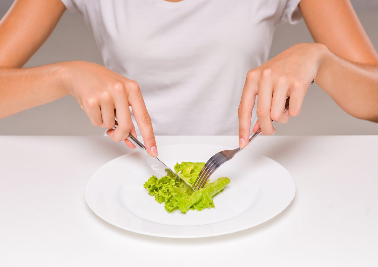 Vrouw snijdt een blad groene sla op haar bord. Alleen armen en bovenlichaam zijn zichtbaar