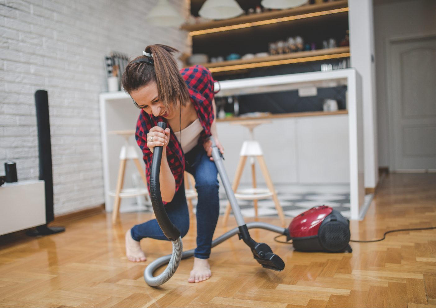 Jonge vrouw is dansend haar huis aan het stofzuigen, gebruikt stofzuigerslang als microfoon en zingt mee