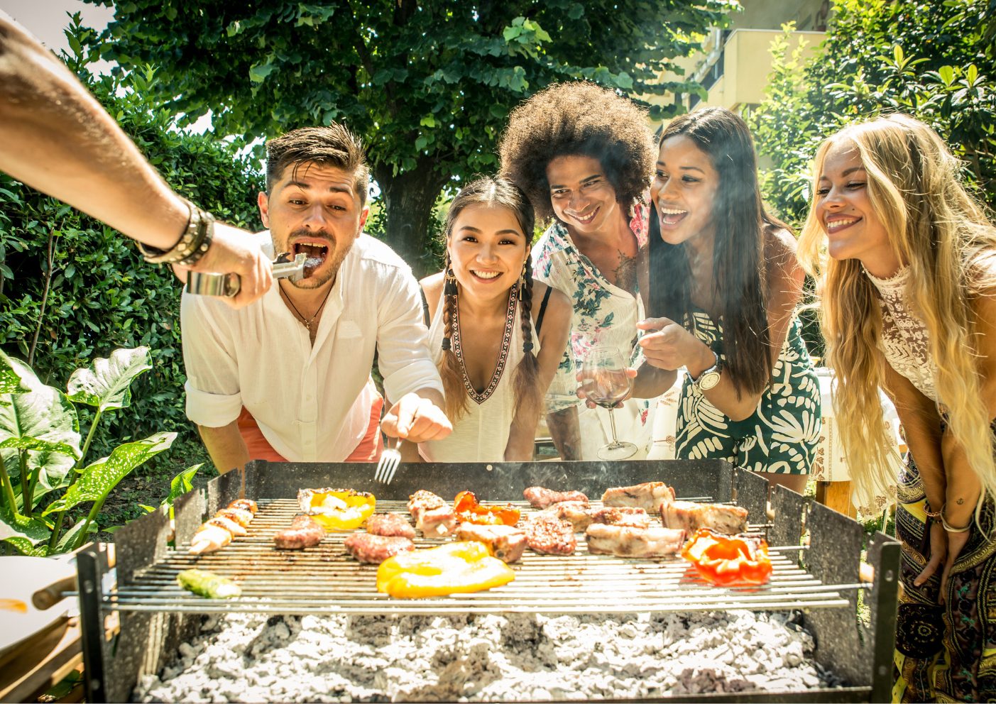 5 vrienden staan bij een BBQ, wachten lachend op een stukje vlees. Een man krijgt alvast een hapje. Zo is er een mannenarm te zien die een vrok vasthoudt met een stuk eten eraan.