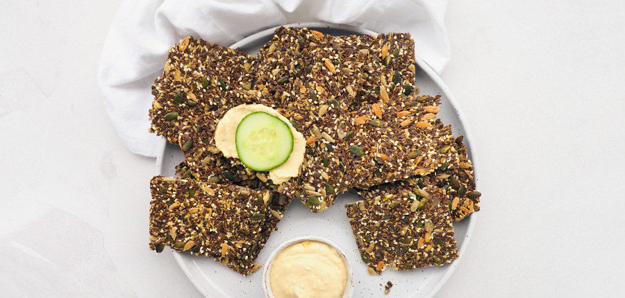 Bord met koolhydraatarme crackers, met klein bakje hummus erbij met een schijfje komkommer