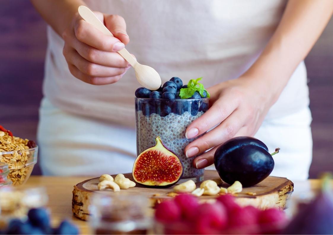 Vrouw haar rechter hand doet een lepel in een glas yoghurt met fruit