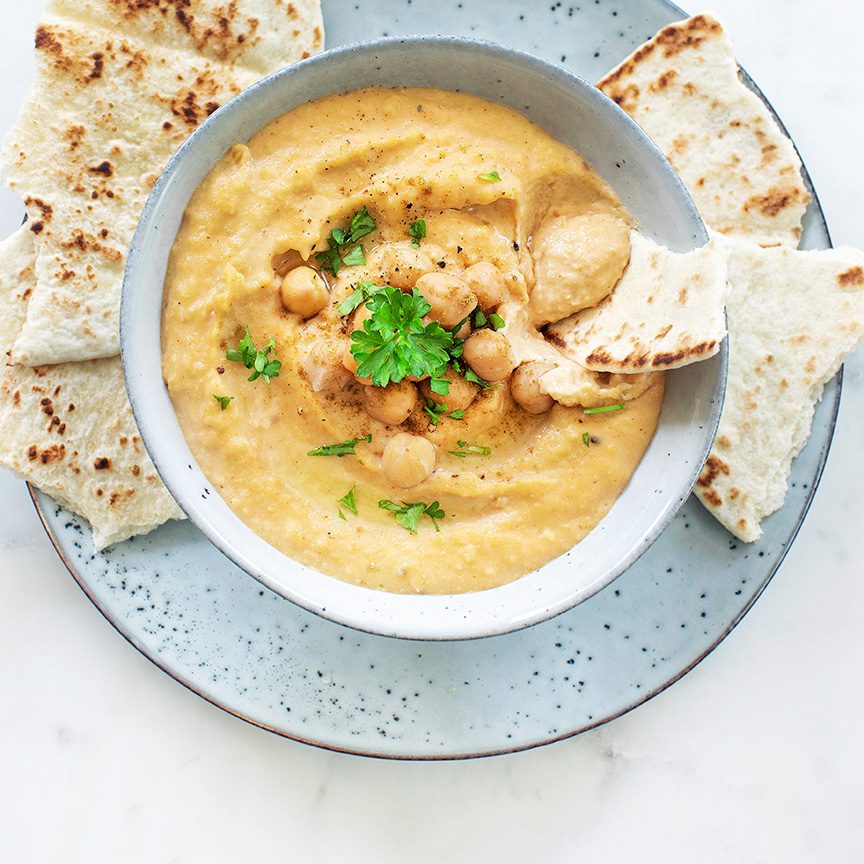 Kommetje met zelfgemaakte hummus met op een bord naanbrood