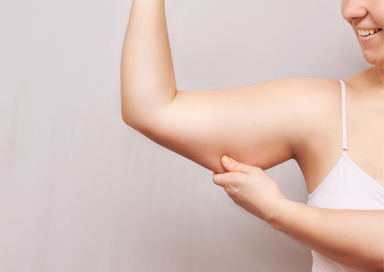 Vrouw houdt haar arm omhoog en het kwabje van haar blote onderarm lachend vast