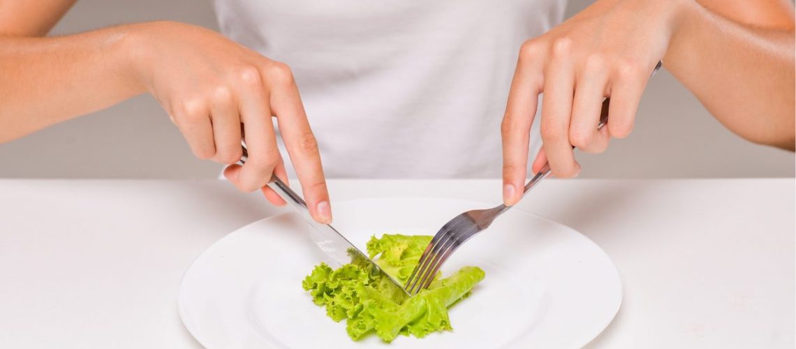 Vrouw snijdt een blad groene sla op haar bord. Alleen armen en bovenlichaam zijn zichtbaar