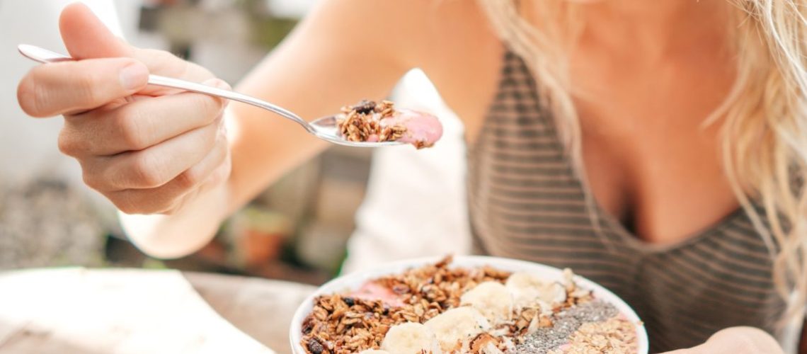 Dame ontbijt met een smoothie bowl. Is bezig een hapt te nemen van haar ontbijt, brengt de lepel naar haar mond