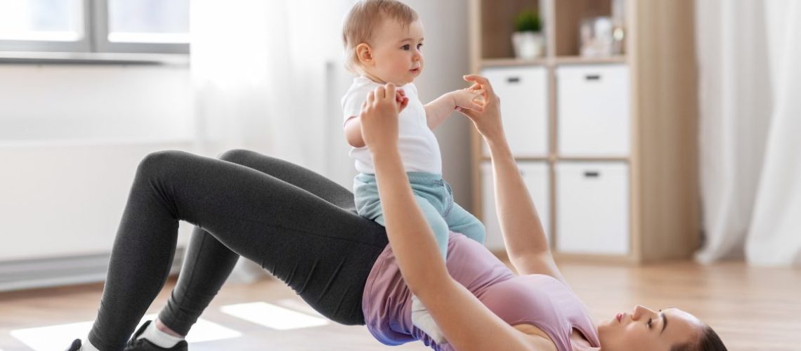 Vrouw traint met kind op buik in woonkamer