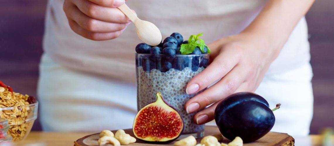 Vrouw haar rechter hand doet een lepel in een glas yoghurt met fruit